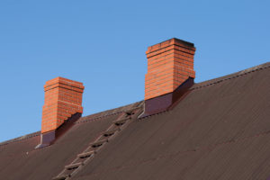 double masonry chimney on house roof against blue sky