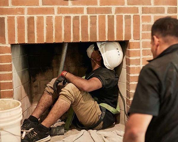 Chimney technician sitting in fireplace firebox performing chimney service