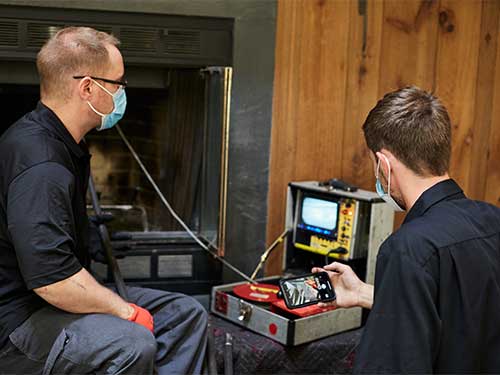 Two technicians performing digital chimney inspection through fireplace