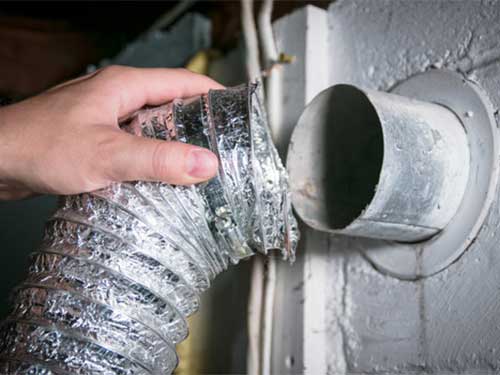 Close up view of technician's hand pulling dryer vent hose from the wall connection