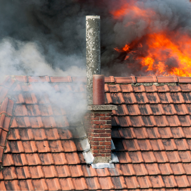 Smoking chimney with a tile roof on fire in the background.