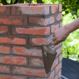 a mason applying mortar to a masonry chimney