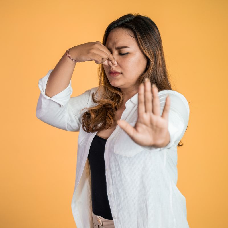 a girl against an orange background holding her nose like something smells bad