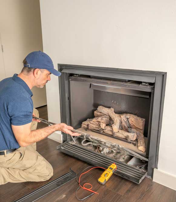 Tech testing gas fireplace insert wearing blue hat and shirt with digital equipment sitting to his right.