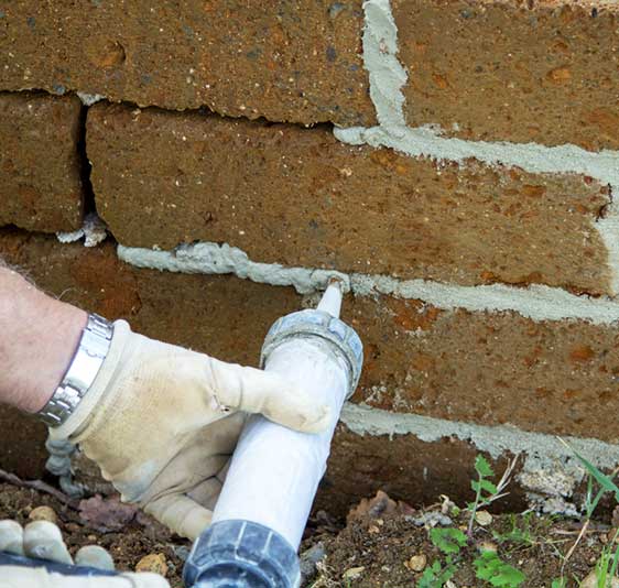 Tuckpointing a brick chimney with an applicator. Techs hand with glove wearing a watch.