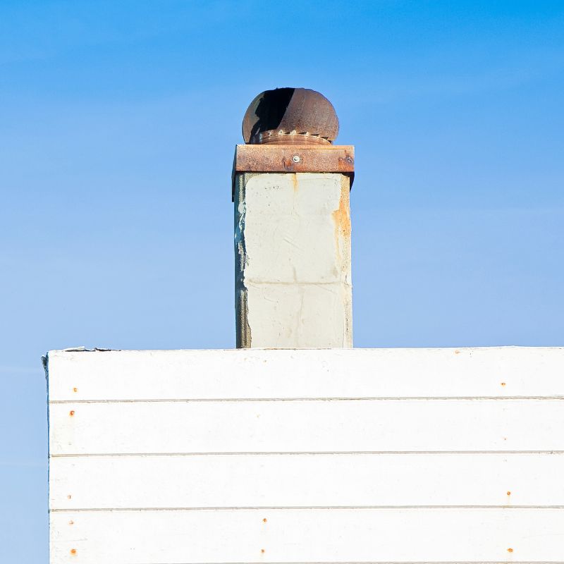 a rusty chimney coming out of a white chase